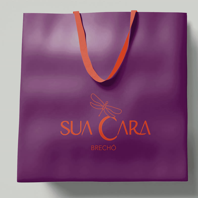 Sacola roxa do brechó Sua Cara com o logo em laranja e a libélula